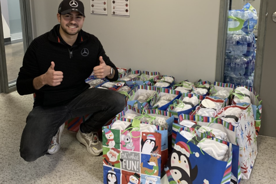 Young man giving two thumbs up with 25 gift bags filled with blankets on the floor next to him