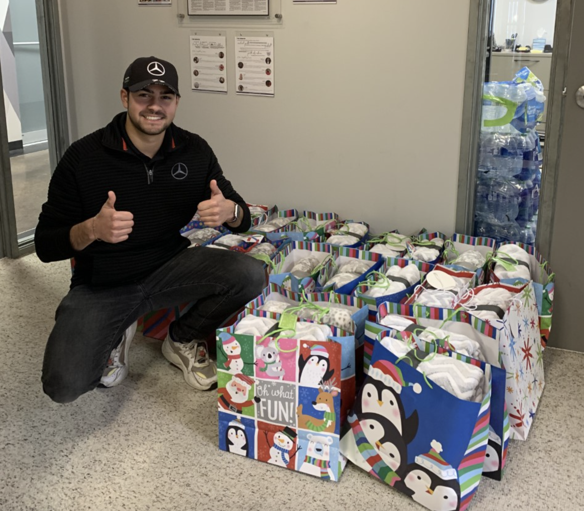 Young man giving two thumbs up with 25 gift bags filled with blankets on the floor next to him